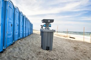 row of portable toilets on a beach with a hand washing station